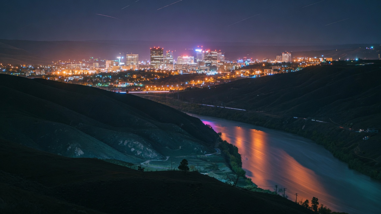 A city glowing in a dark river valley at night